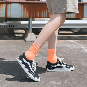 Orange velvet crew socks for women styled with black sneakers on industrial background
