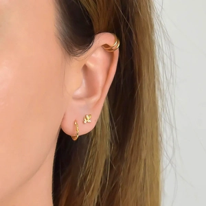Close-up of golden leaf stud earrings and layered ear cuff set on model's ear