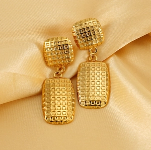 Macro detail of gold-plated square earrings with textured grid patterns on silk fabric