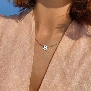 Minimalist gold beaded necklace featuring a natural shell letter B pendant on a model