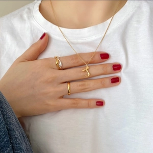 Close-up of gold T-pendant necklace and wave ring set on a model with white t-shirt