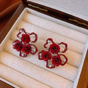 Detailed close-up of red rose earrings with pearls and rhinestones on a wooden background