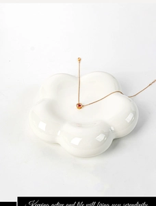 Close-up of a gold necklace with red gemstone pendant on a white floral ceramic tray