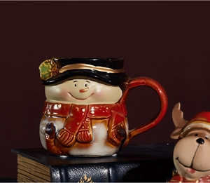 Close-up of ceramic snowman Christmas mug with red scarf and hat on vintage books