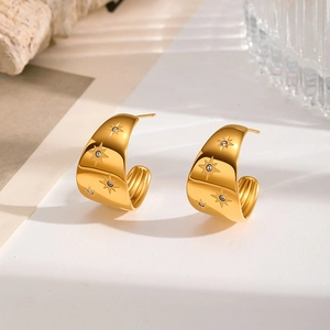 Detailed view of C-shaped gold earrings with star patterns and sparkling zircon stones