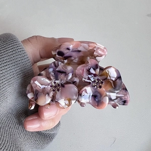 Close-up of a floral acetate hair claw with purple marble texture and rhinestone center
