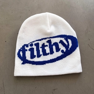 Detail of white knit beanie featuring blue filthy jacquard text on industrial floor