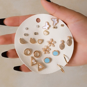Close-up of 12 pairs gold stud earrings with pearls and crystals on a white card