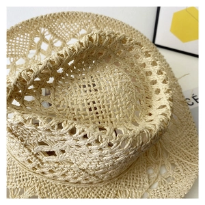 Close-up of a beige hand-woven straw cowboy hat with intricate hollowed-out patterns
