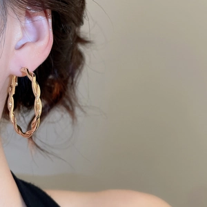 Detail of a gold twisted hoop earring shown on a model with a smooth metallic texture