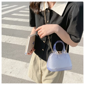 Blue transparent PVC shell bag with golden chain strap worn by a model outdoors