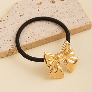 Detail of a minimalist gold metal bow hair tie with textured finish on a stone background