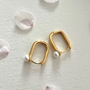 Elegant U-shaped gold-plated pearl hoop earrings on a minimalist floral background