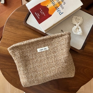 Detail of wool tweed cosmetic bag with woven label on a rustic wooden table setup