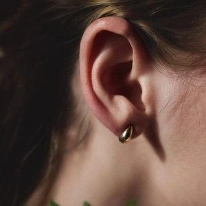 Close-up of polished 18K gold waterdrop stud earrings worn on ear for elegant display
