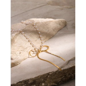 Detailed macro of gold bow pendant on pearl chain necklace against a stone surface
