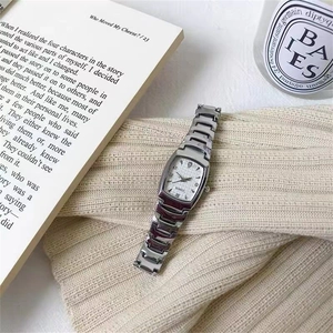 Silver tonneau watch with crystal hour markers on a beige sweater background