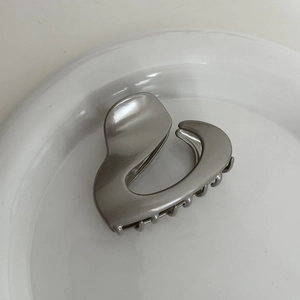Macro shot of silver metallic heart-shaped hair claw clip on a white decorative dish