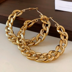 Detail of high-polish chunky gold chain link hoop earrings on a minimalist wooden tray