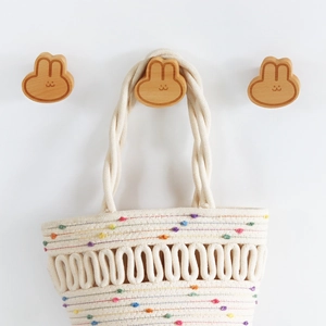 Three minimalist wooden rabbit wall hooks with natural texture holding a woven bag
