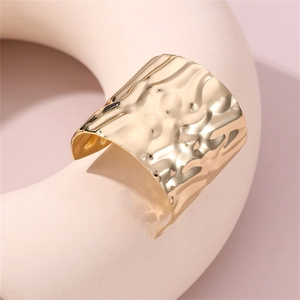 Detail shot of a wide gold metal cuff bracelet featuring a textured hammered finish