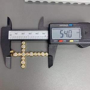 Close-up of a 54mm gold cross pendant with clear crystals measured by digital caliper
