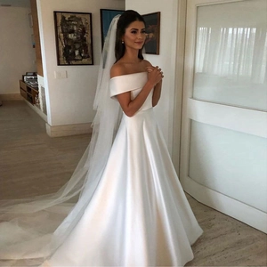 Detail of off-the-shoulder white satin wedding dress with long tulle veil and A-line skirt