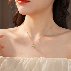 Close-up of gold plated necklace featuring a teal cat-eye cube pendant on a model's neck