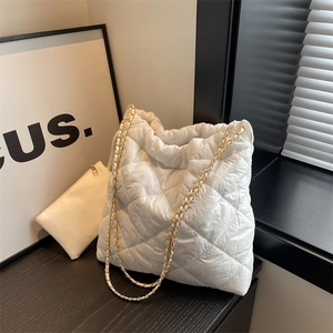 White quilted large tote bag with chain strap and matching pouch on wooden desk