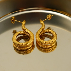 Close-up showing the detailed scale texture of gold snake stud earrings on a tray