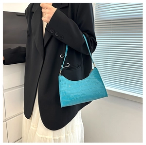 Detail of bright blue crocodile pattern underarm bag on model with black blazer