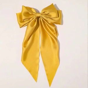 Close-up of a glossy yellow satin bow hair clip with elegant long ribbons for women