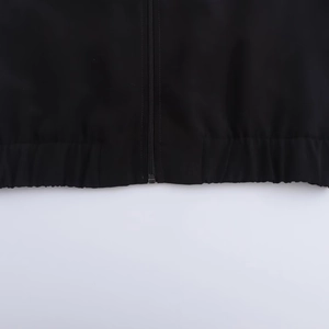 Detail view of the black sweatshirt hem featuring a metal zipper and elastic waist design