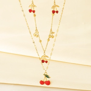 Detail of layered gold chain necklace featuring red enamel cherry and heart pendants