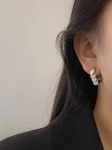Macro detail of silver layered metal hoop earrings with round charms on model