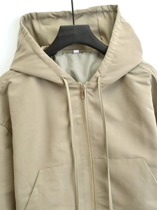 Detail of hooded jacket with metal zipper closure and adjustable drawstrings in khaki color