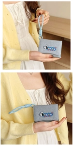 Close-up of grey denim wallet with cartoon embroidery and matching woven wrist strap
