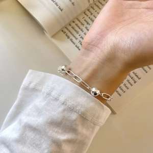 Minimalist silver bead and paperclip link bracelet worn over an open book