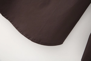 Detail view of the curved hem and fine stitching on a brown poplin long sleeve shirt