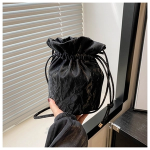 Detail of black drawstring bucket bag with shiny pleated texture and soft natural light