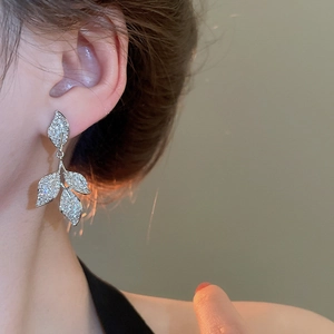 Detailed view of silver leaf tassel earrings with sparkling cubic zirconia on model