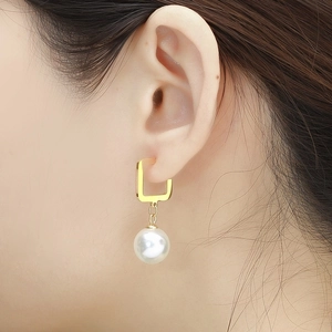 Close-up of a square gold earring with a white pearl pendant worn on the ear