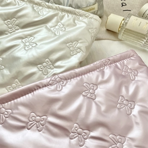 Close-up of quilted PU makeup pouches in silver and pink with embossed bow patterns