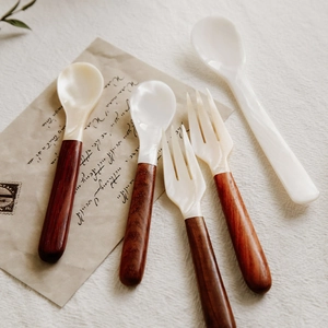 Close-up of elegant white shell cutlery set with textured redwood handles on vintage paper