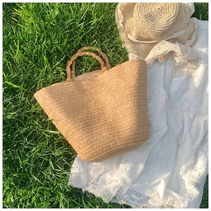 Detail of handwoven straw tote with natural bamboo handles on green grass background
