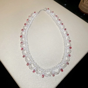 Detail of beaded lace necklace with white beads and red teardrop pendants on white surface