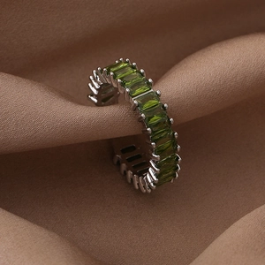 Macro shot of silver ring with green baguette-cut zircons on soft silk fabric