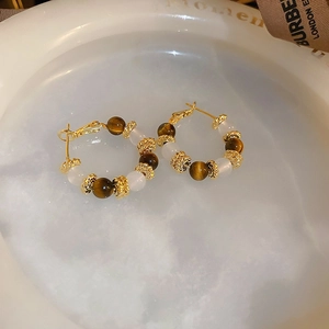 Detailed shot of retro tiger eye stone and white chalcedony earrings in a ceramic dish