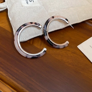 Detail of leopard print resin and silver C-shaped hoop earrings on a textured fabric