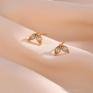 Detailed view of gold plated leaf earrings with marquise cut zircon on pink silk fabric